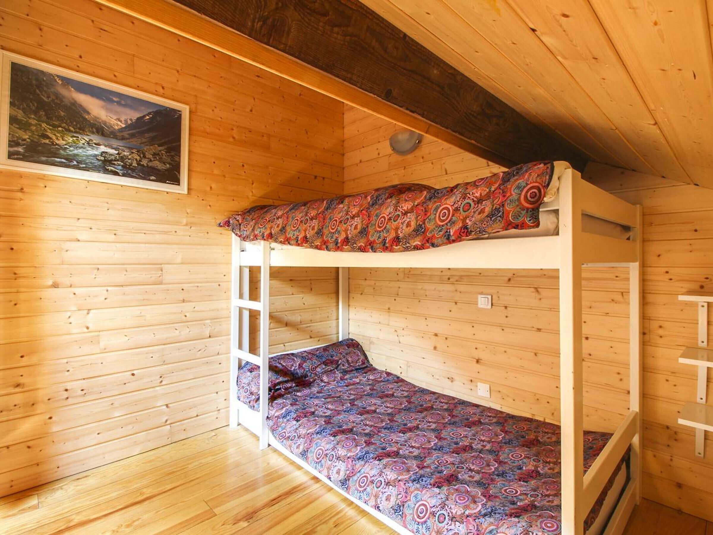 A wooden cabin room with a bunk bed, a painting of a mountain landscape, and a wooden floor.