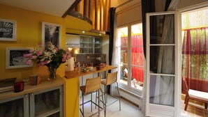 Una cocina acogedora con barra de madera, paredes amarillas y un ventanal con cortinas rojas.