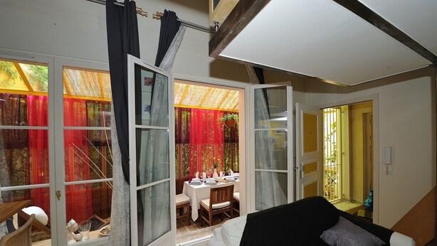 Una habitación con una cama, una mesa de comedor lista para dos personas y vistas a un comedor por una puerta abierta.