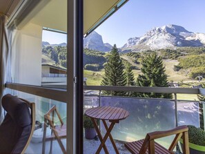 Un balcon donnant sur un paysage montagneux, avec des meubles en bois et une porte vitrée.