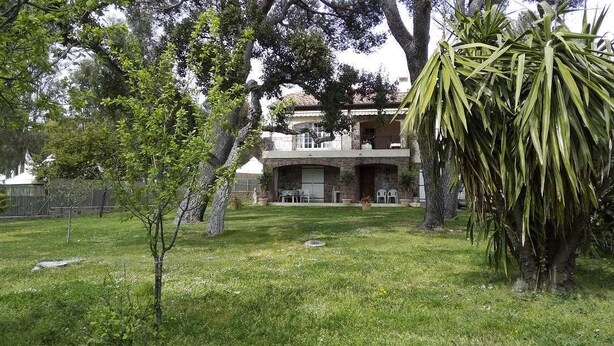 A two-story house with a balcony, surrounded by a grassy lawn and trees.