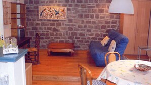 A cozy living room with a stone wall, a blue sofa, a wooden coffee table, and a dining table with a floral tablecloth.