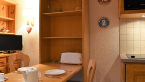 Et spiseområde med et træbord, stole, en hvid tepotte og et fjernsyn på et træskab.