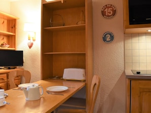 Ruokailutila, jossa on puinen pöytä, tuoleja, valkoinen teekannu ja televisio puisen kaapin päällä.