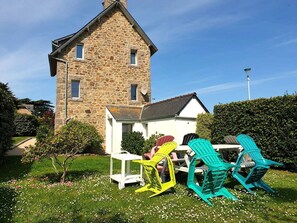 A stone building with a white annex, outdoor seating with colorful chairs, and a small table.