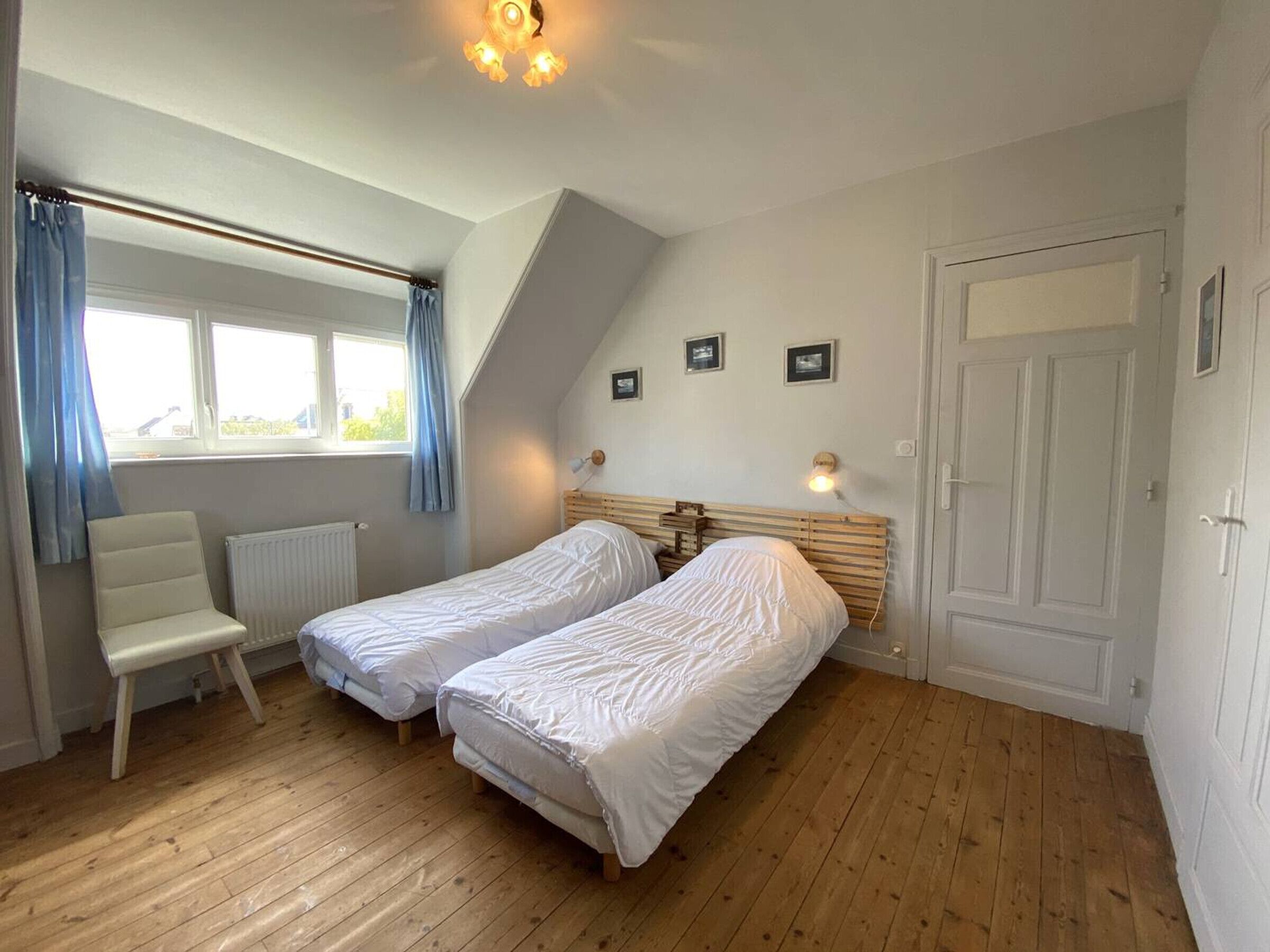 A bedroom with two single beds, a chair, a radiator, and a window with curtains.