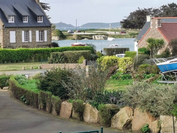 A coastal area with a stone building, a paved road, and a body of water with boats.