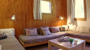 A cozy room with wooden walls, a sofa set, a coffee table, and two windows with curtains.