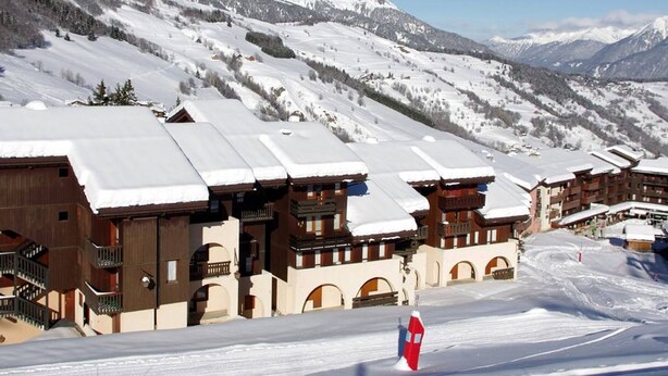 A snow-covered mountain resort with chalet-style buildings, ski slopes, and a clear sky.