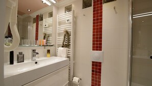 A modern bathroom with a glass shower enclosure, a white sink with a gold faucet, and a red-tiled accent wall. - E4GG So sweet (París)
