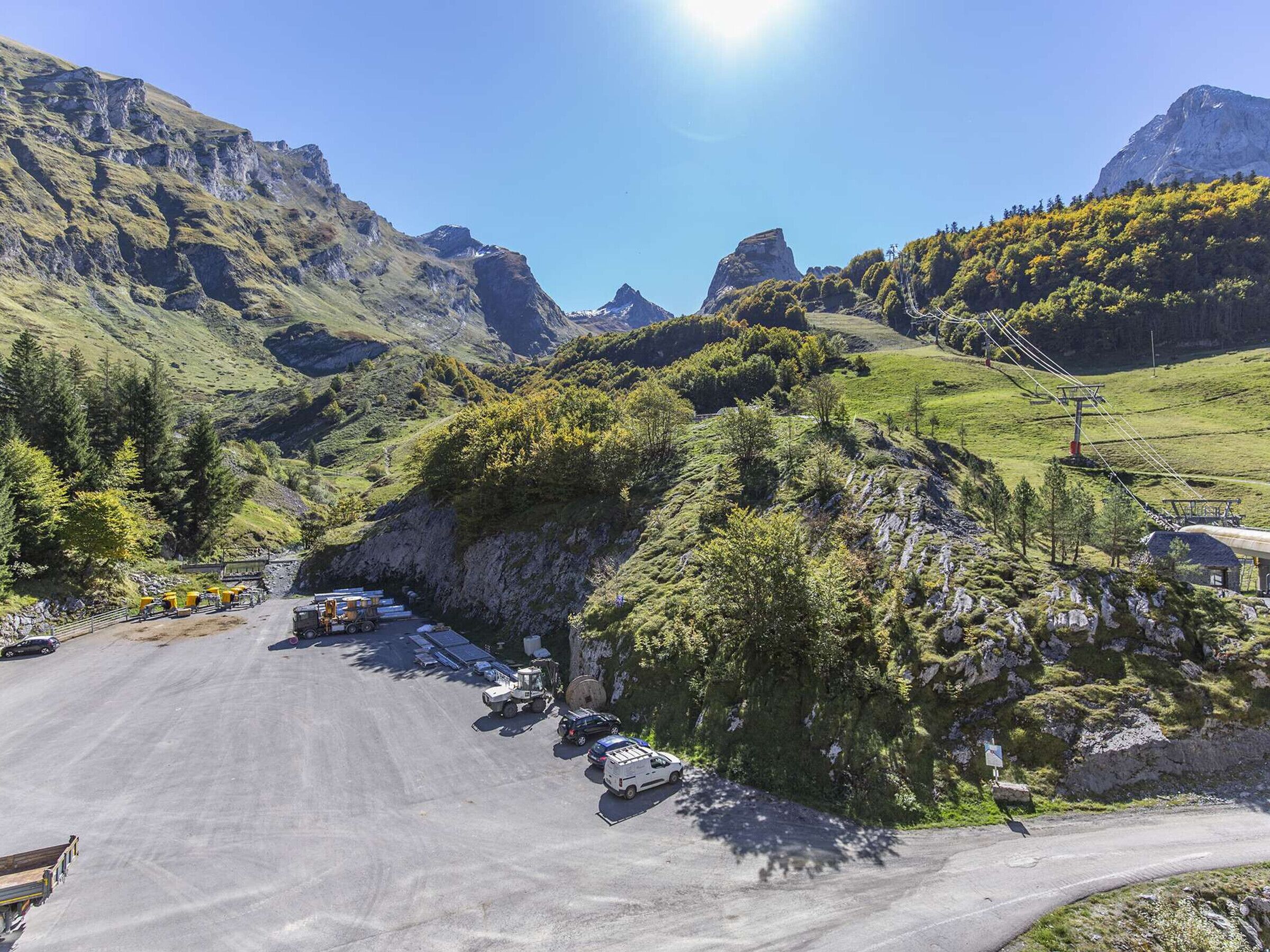 A mountainous landscape with a paved road, parked vehicles, and a small building with a sloped roof.