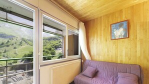 Une pièce avec un canapé violet, de grandes fenêtres donnant sur un paysage verdoyant, un plafond en bois et un tableau encadré accroché au mur.