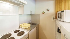 Une cuisine de taille réduite, avec des meubles blancs, une cuisinière, un four à micro-ondes et un évier.