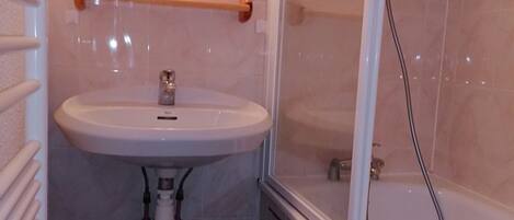 Un baño con lavamanos blanco, un espejo y cabina de ducha.