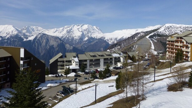 A hotel complex with multiple buildings, a parking area, and a view of snow-covered mountains. - Cozy Studio for 4 in Alpe d'Huez, Close to Slopes & Shops, Balcony, Pets Welcome (Huez)