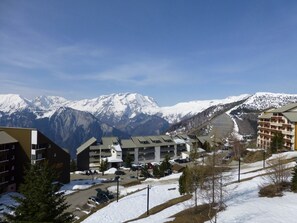 A hotel complex with multiple buildings, a parking area, and a view of snow-covered mountains. - Cozy Studio for 4 in Alpe d'Huez, Close to Slopes & Shops, Balcony, Pets Welcome (Huez)