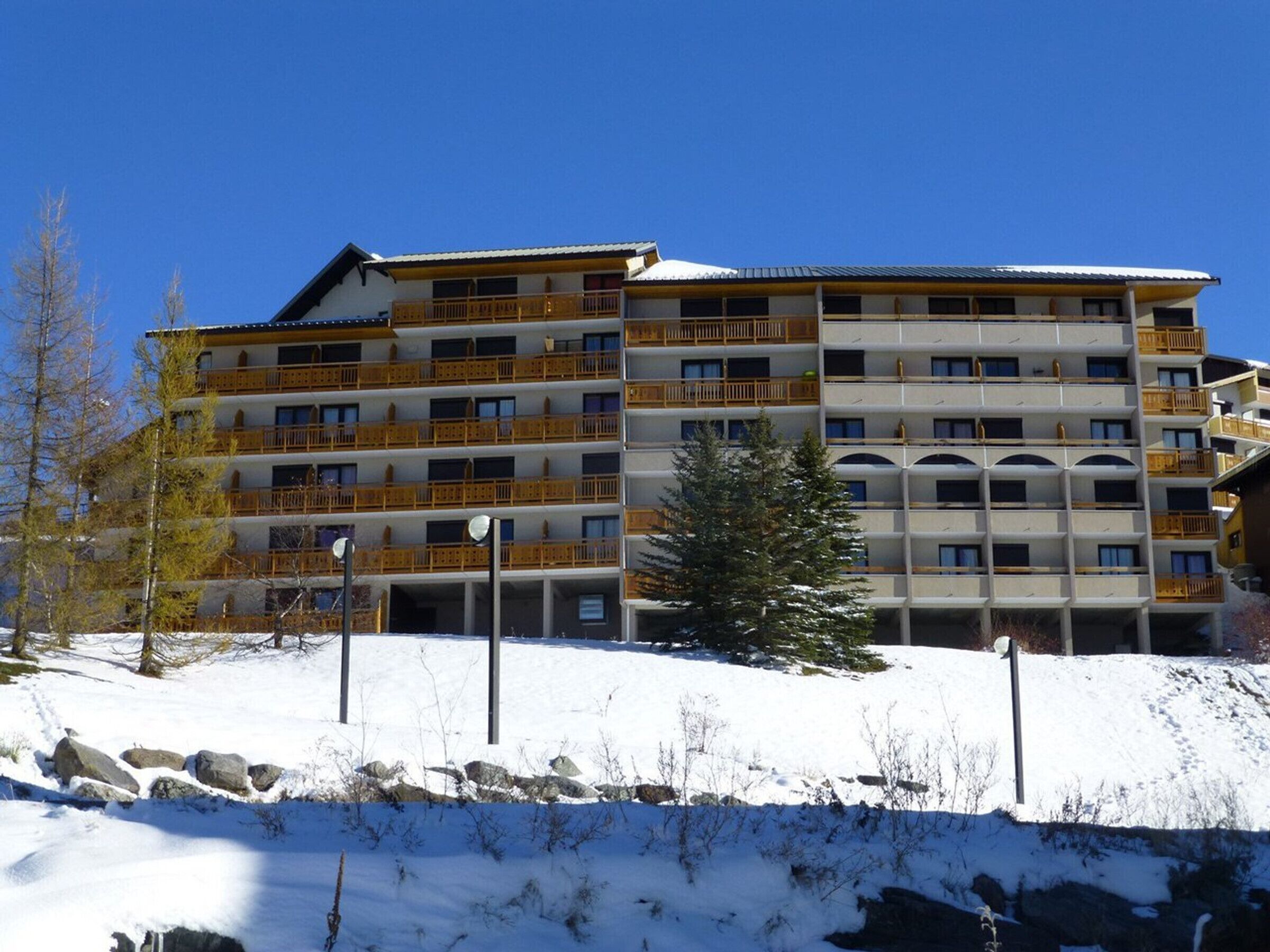 Un hotel de varios pisos con balcones, una pista de esquí al frente y un cielo azul despejado.