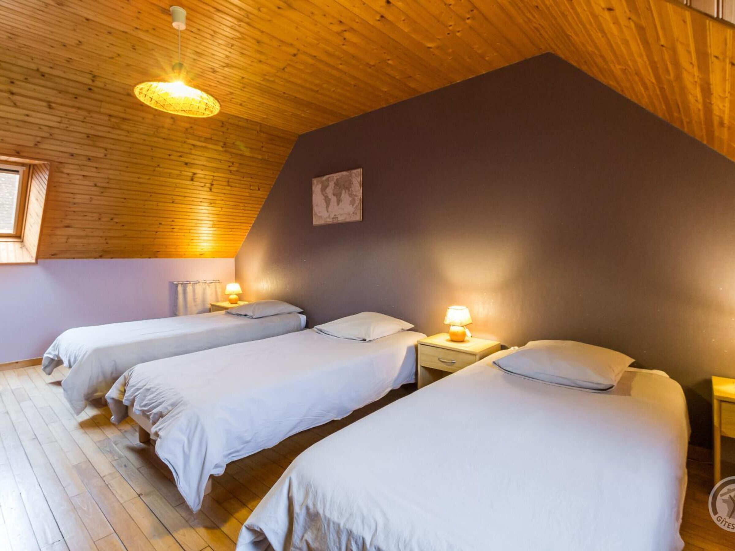 Une pièce chaleureuse avec trois lits alignés contre un plafond en pente, un plancher en bois et une carte du monde accrochée au mur.