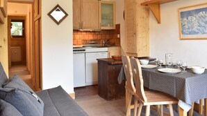 A cozy kitchen with wooden cabinets, a dining table set for four, and a view of the adjacent living area. - Cozy 2-Room Apt for 4, 100m from Slopes, Balcony, Pet-Friendly, WiFi - Méribel (Méribel)