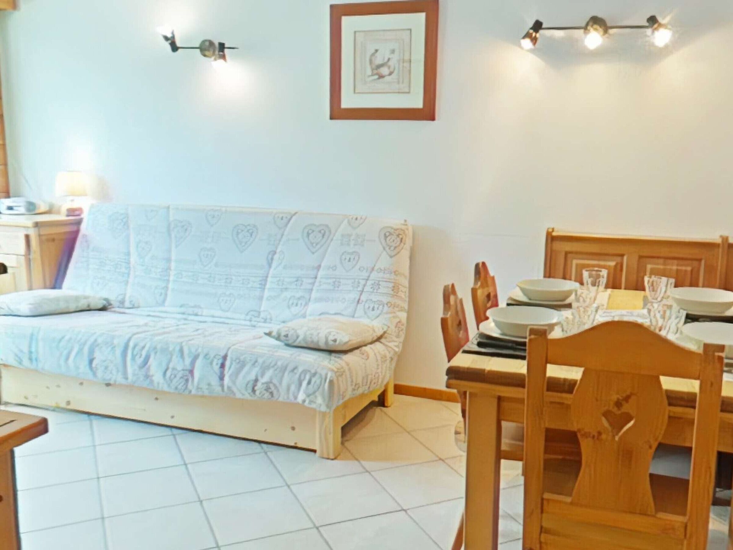 A room with a bed, a dining table with chairs, a wall-mounted light fixture, and a framed picture.