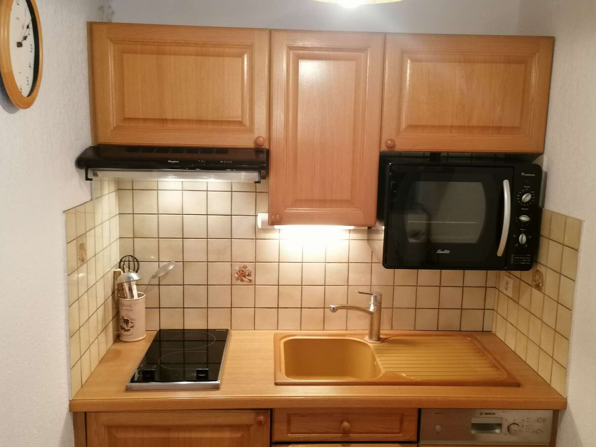 A kitchen with wooden cabinets, a black microwave, a sink, and a Bosch dishwasher.