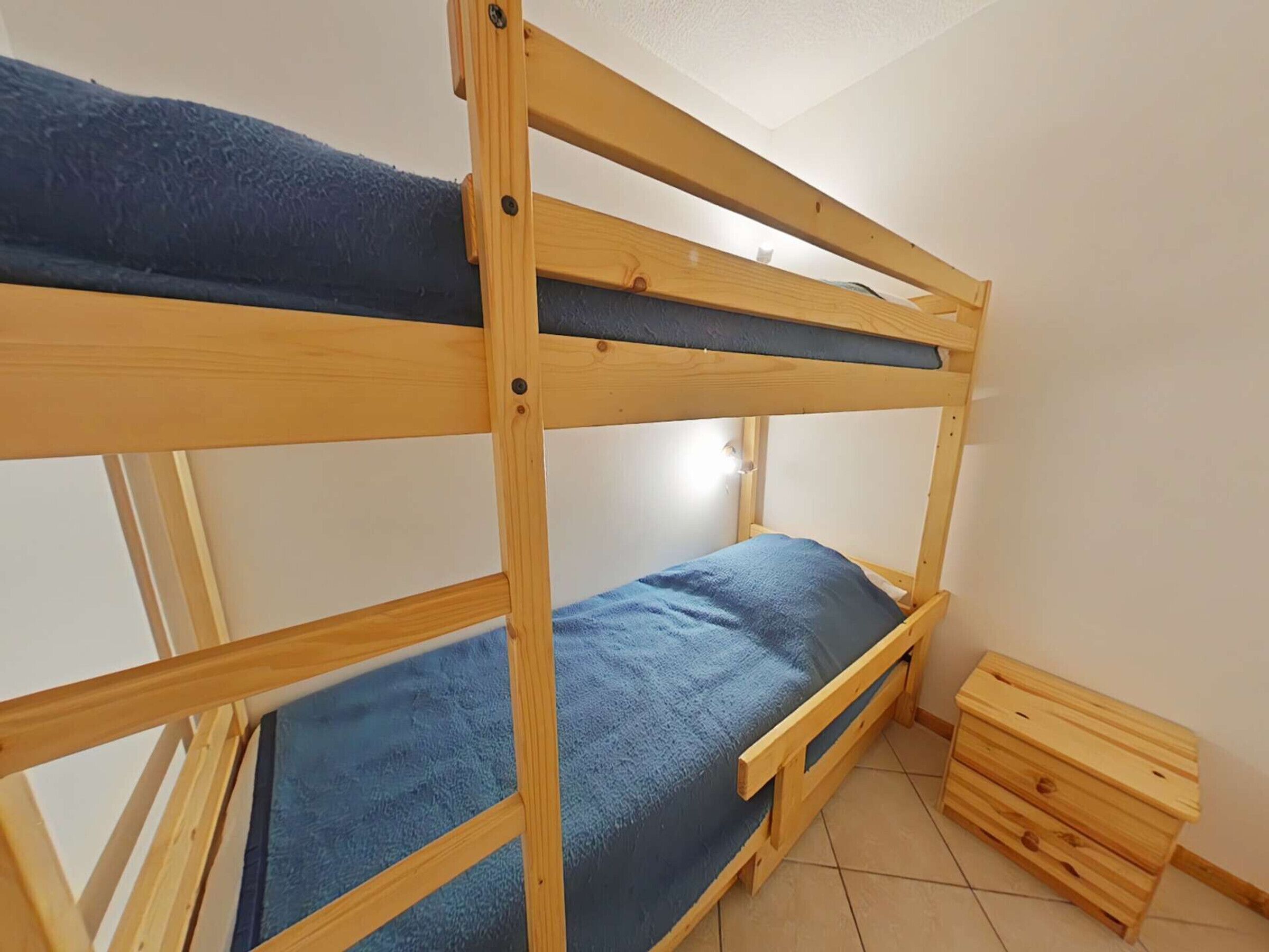 Ein Etagenbett mit blauer Matratze in einem Raum mit weißen Wänden und Fliesenboden.