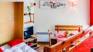 A cozy hotel room with a bed, a TV, a small table with fruit, and a red wall.