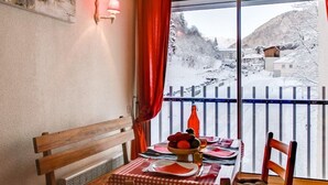 A dining area with a table set for two, a wooden bench, and a view of a snowy landscape through a balcony.