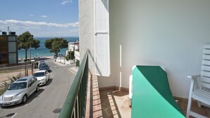 A balcony with a view of the sea and parked cars.