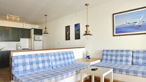 A living room with a sofa set, a small table, and a kitchen in the background.