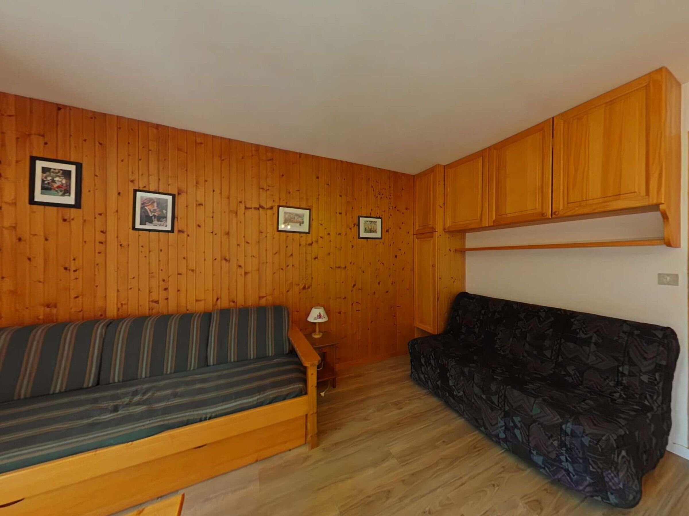 Une pièce aux murs recouverts de lambris en bois, avec un canapé à rayures, un canapé à motifs et une petite table sur laquelle se trouve une lampe.