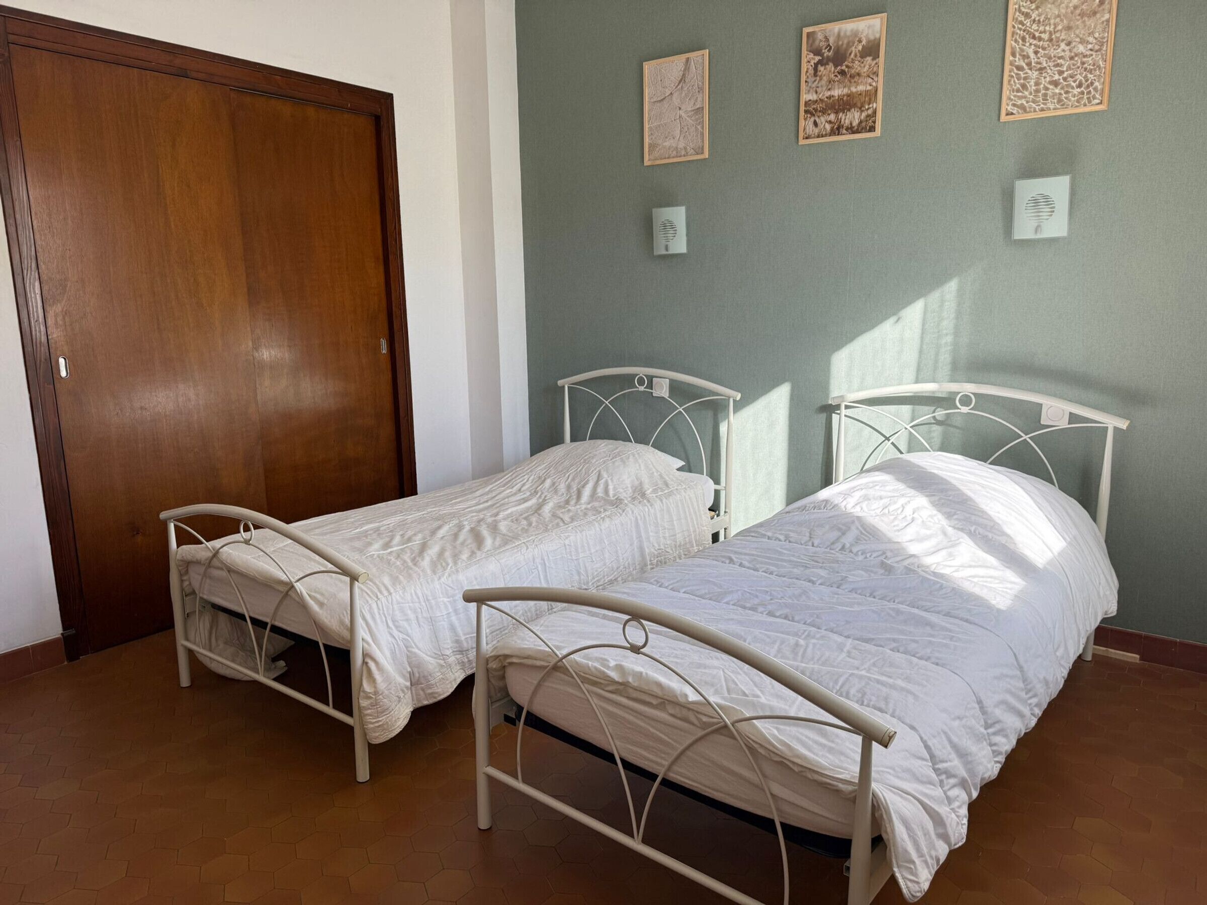 A room with two single beds, a wooden door, and three framed pictures on the wall.