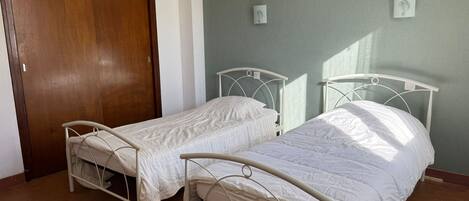 A room with two single beds, a wooden door, and three framed pictures on the wall.