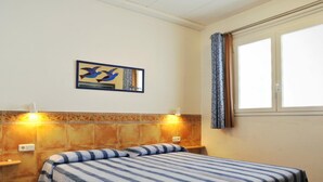 Una camera d'albergo con due letti, una parete decorata con un dipinto di uccelli, una finestra con tende e un muro rivestito di piastrelle.