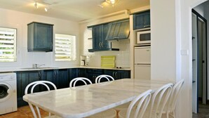 Una cucina moderna con mobili blu scuro, un piano di lavoro bianco, un forno integrato e un'area pranzo con tavolo in marmo e sedie bianche.