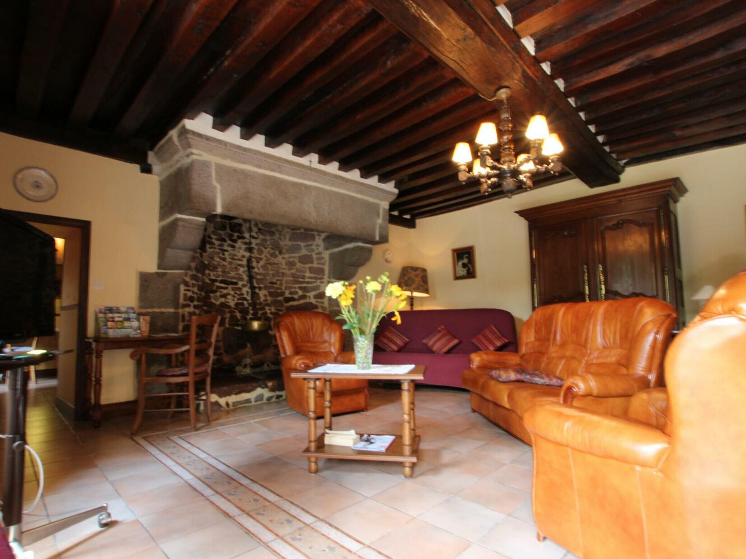 A cozy living room with leather furniture, a stone fireplace, and a chandelier.