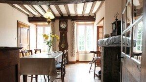 Een traditionele eetkamer met een geruit tafelkleed, houten stoelen, een hanglamp en een stenen openhaard.