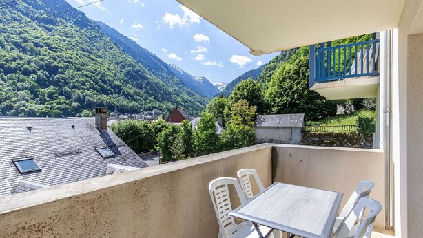A balcony with a table and chairs, overlooking a mountainous landscape with a village below. - Apartment Cauterets, 1 bedroom, 4 persons (Cauterets)