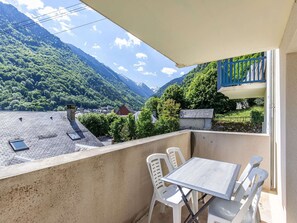 Ein Balkon mit Tisch und Stühlen, der auf eine gebirgige Landschaft mit einem Dorf weiter unten blickt.