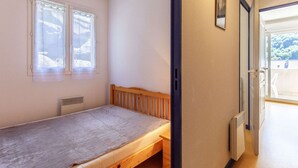 A small, single-bed room with a wooden headboard, a radiator, and a window with sheer curtains. - Apartment Cauterets, 1 bedroom, 4 persons (Cauterets)