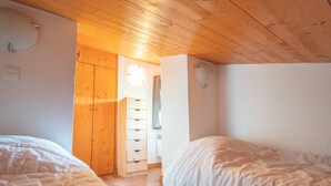 Un dormitorio con dos camas, suelo de madera, un armario y un ventanal pequeño.