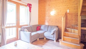 Una habitación acogedora con un sofá gris, una escalera de madera y suelo de madera.
