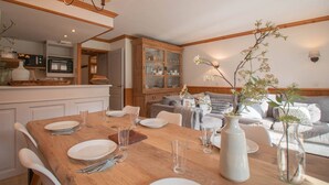 A dining area with a wooden table set for four, a kitchen in the background, and a living area with a sofa and decorative plants. - Renovated 4-room duplex, 6 pers., 2 balconies, ski locker, cleaning included (Valmorel)