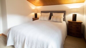 A bedroom with a wooden ceiling, a large bed with white bedding, two bedside tables with lamps, and a wooden nightstand with drawers. - Renovated 4-room duplex, 6 pers., 2 balconies, ski locker, cleaning included (Valmorel)