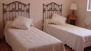Two single beds with metal headboards, a bedside table with a lamp, and a window with curtains.