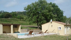 A pool area with lounge chairs, a small building with a satellite dish, and a large tree in the background.