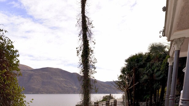 A pathway leading to a body of water with a view of mountains in the background. - Casa Punta Amore - WelcHome (Cannobio)