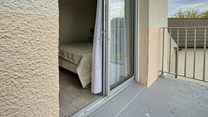 En balkon med en skydedør, der fører ind til et soveværelse med en seng og et natbord.