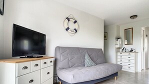 En moderne stue med en grå sofa, et træ-tv-skab, en hvid kommode og en redningskrans som pynt på væggen.