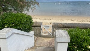 Ein Strand mit Booten im Wasser, ein sandiger Uferstreifen und ein steiniger Weg zum Strand.